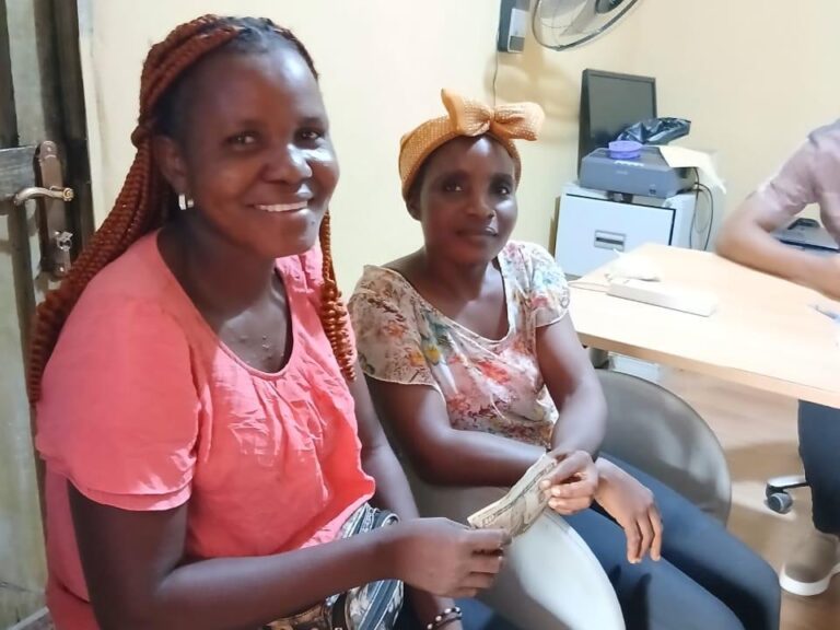 Two women at Mineke Foundation, holding US dollar bills and smiling